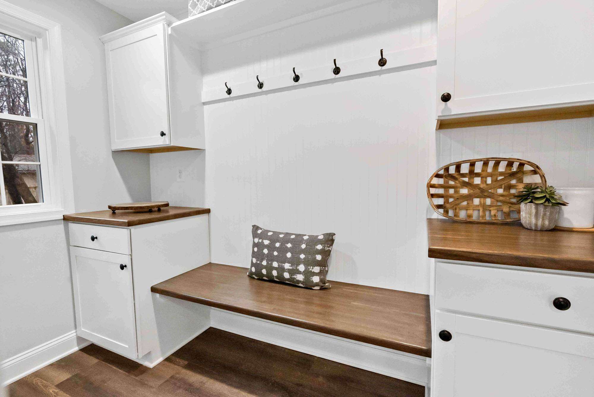White mudroom with brown wood bench and hooks