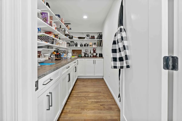 Large, long, walk-in pantry with floating shleves and wood countertop