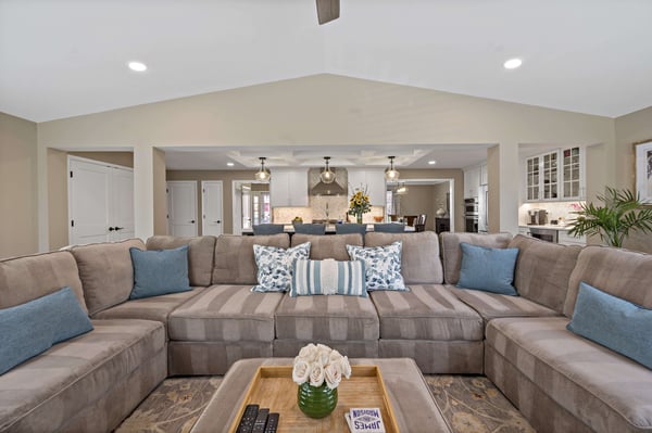 Brown sectional couch in living room with cathedral ceiling and open kitchen in back