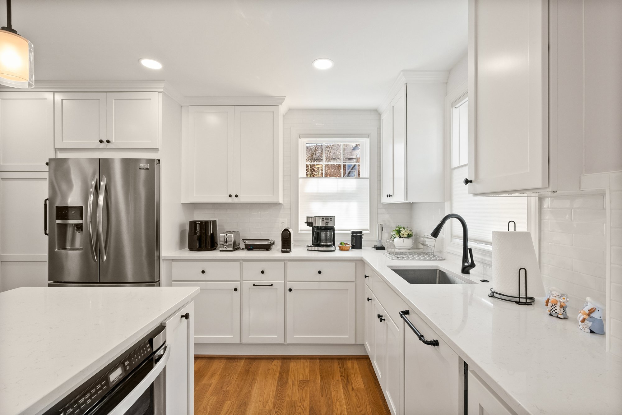 Bright white kitchen remodel in Arlington featuring quartz countertops, black fixtures, stainless steel appliances, and custom cabinetry blending old and new elements.