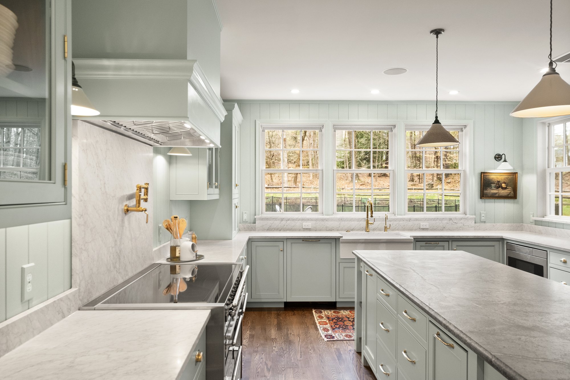 A brightly-lit kitchen with pendant lighting, pot filler, and light cabinets and countertops