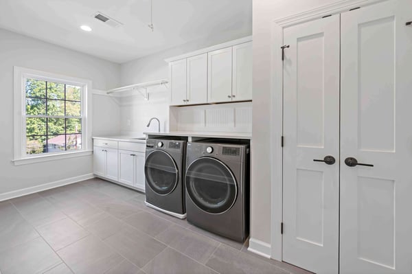 Large, white laundry room with cabinets, closet, and sink