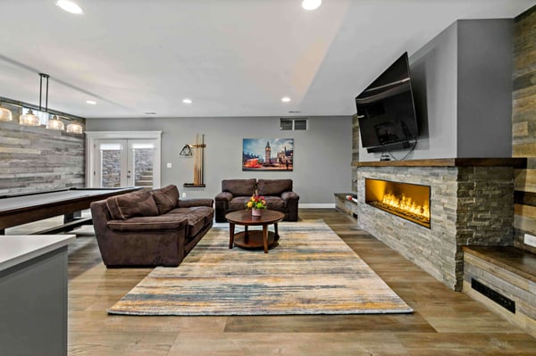 Electric fireplace surrounded by stone and couches in basement
