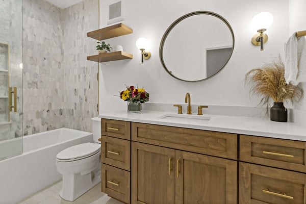 Brown and gold full bathroom with circle mirror and floating shelf