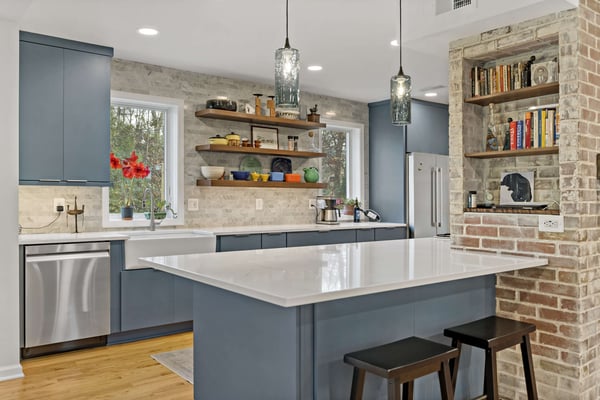 Blue kitchen cabinets with white countertops and exposed brick support wall