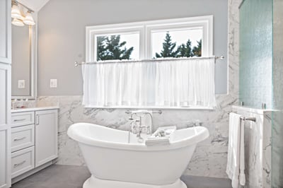 Bathtub and curtains in bathroom with marble walls