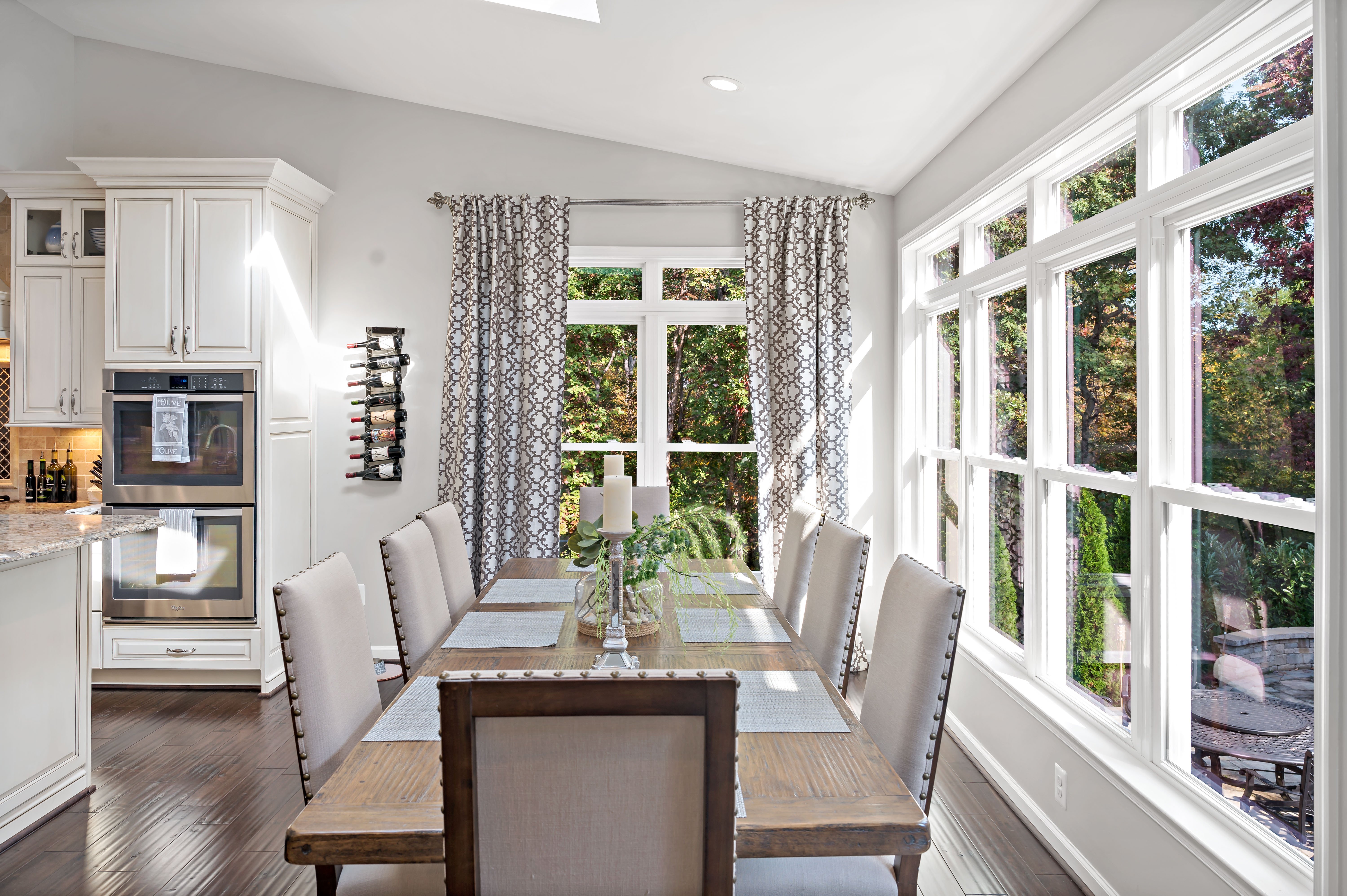 Dining room table with large windows and curtains overlooking backyard