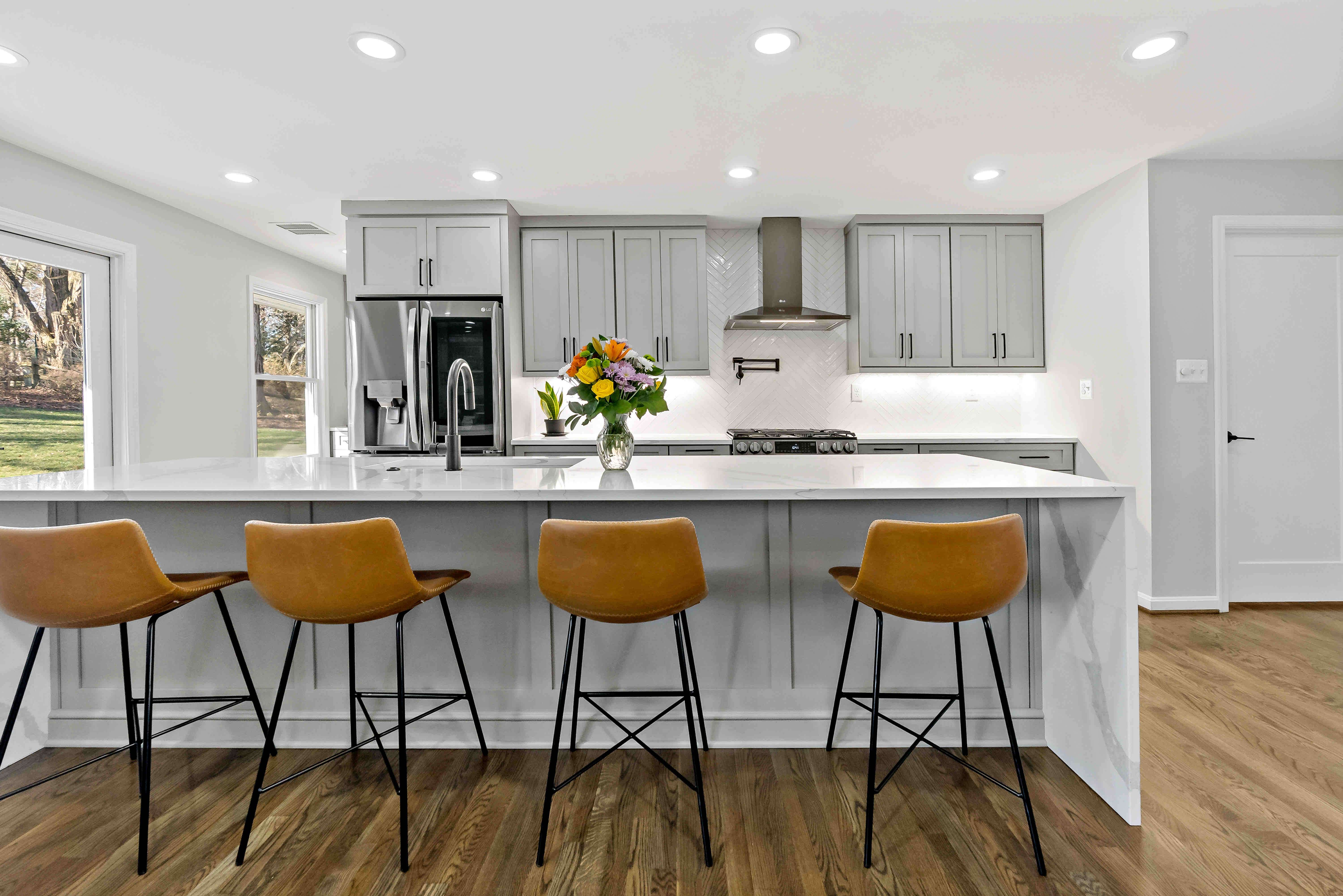 Long white kitchen island with brown chairs for seating