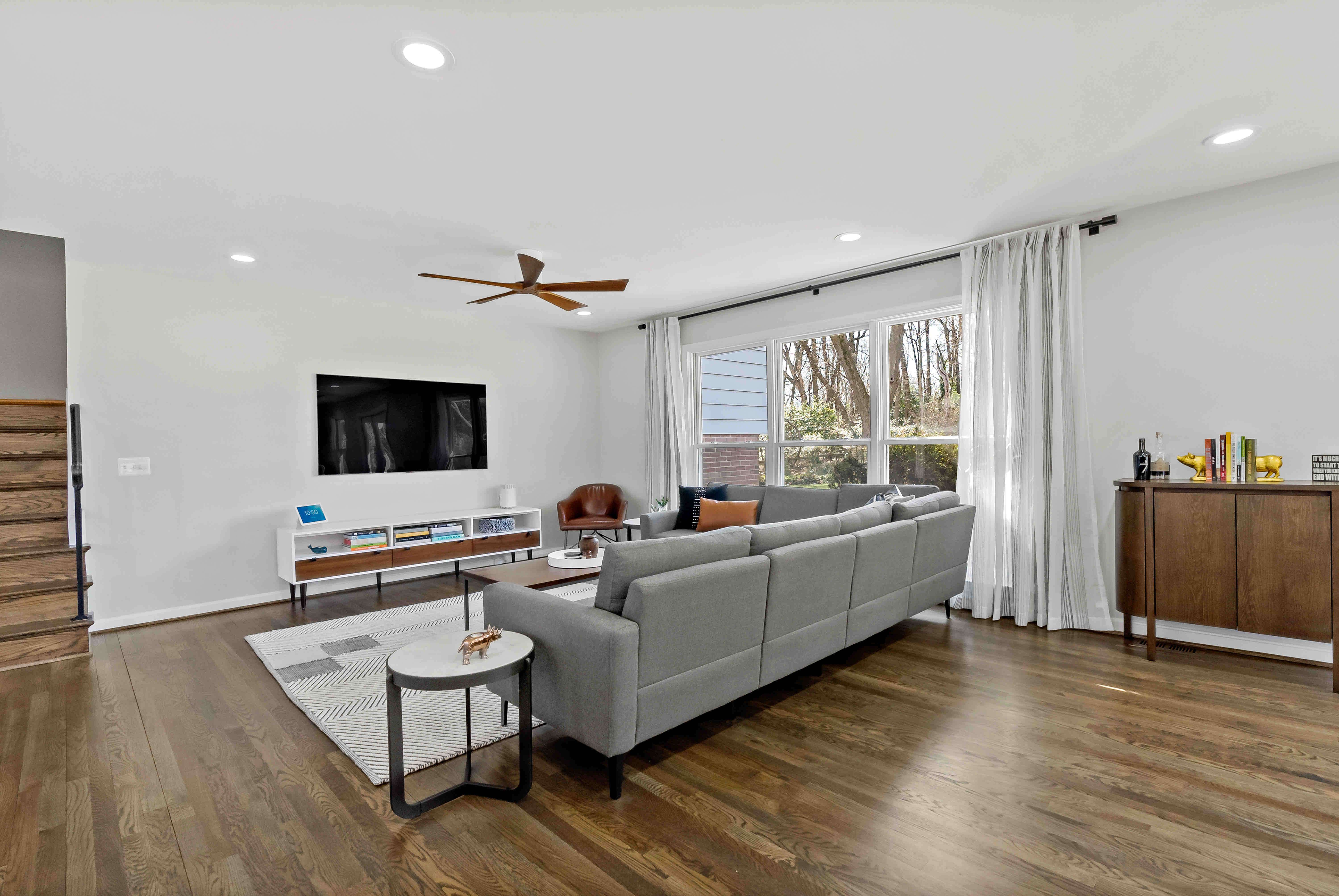 Open living room with ceiling fan and window treatment