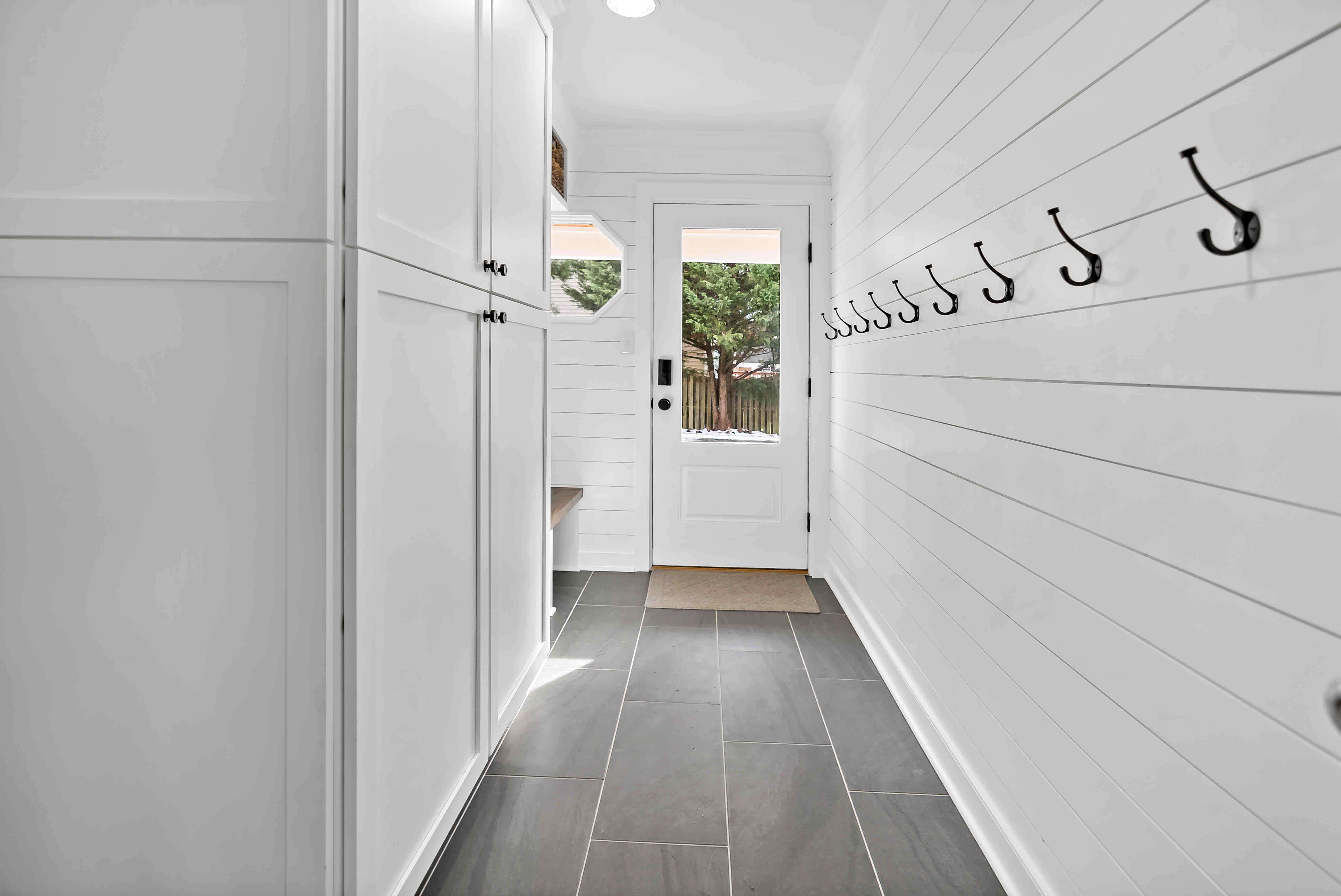 White mudroom with multiple wall hooks to hang jackets