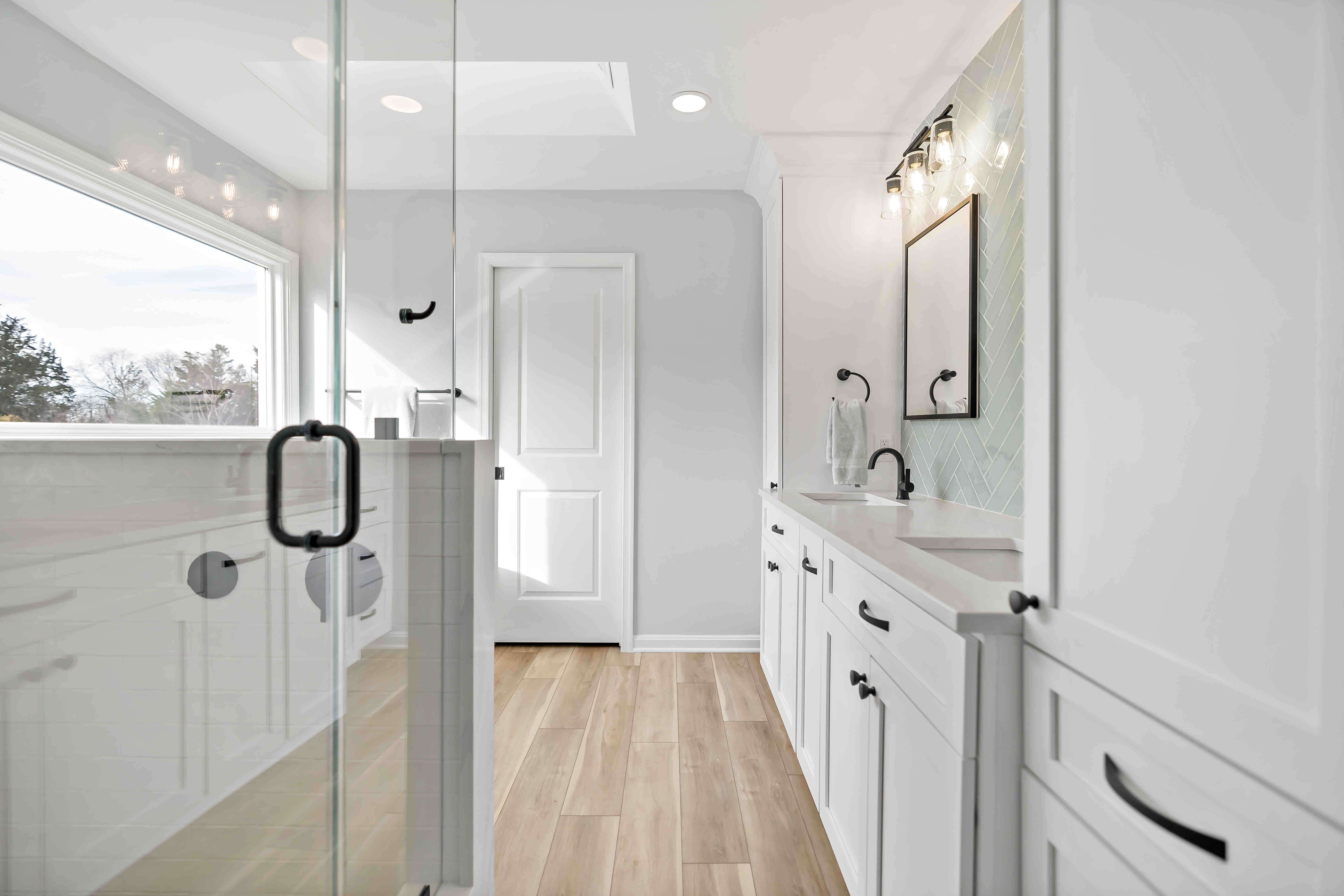 Glass shower door in clean white full bathroom