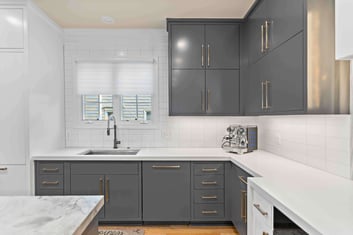 White countertop and backsplash in kitchen with grey cabinets and gold fixtures