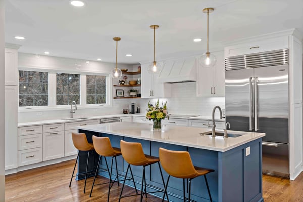 Modern white kitchen with blue island and brown leather chairs