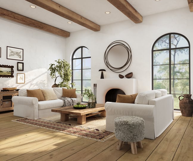 Creamy colored living room with large, rounded windows, lots of natural light, wood beams, and layered textures