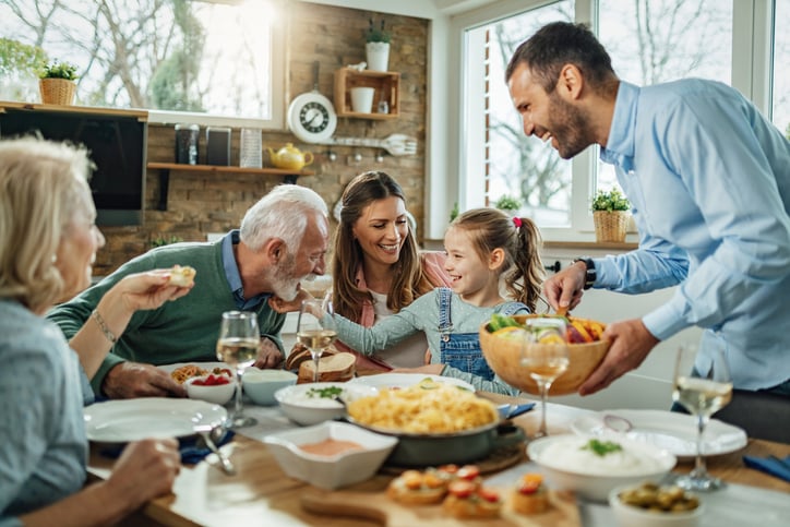 Happy multi-generational family enjoying a meal together at home, smiling and sharing food around a dining table.