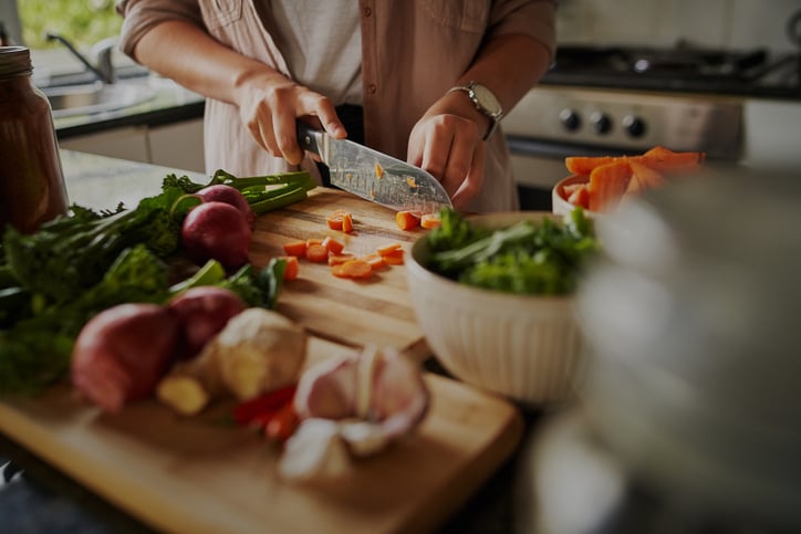 Closeup of young female hands chopping fresh vegetables on chopping board while in modern kitchen 