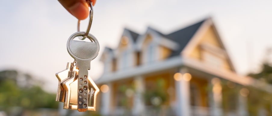Keys to a house dangling with a blurred view of the home in the background
