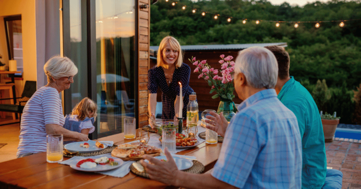 Multigenerational family enjoying indoor outdoor living space by having dinner together in the back yard